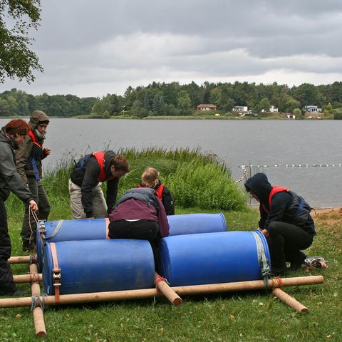 Vier Personen lassen ein selbst gebautes Floß zu Wasser